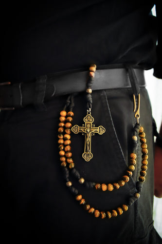 Close-up of a person wearing a black belt with a cross pendant and tiger's eye stone beads.