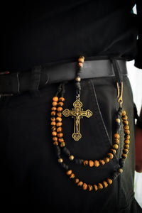 Close-up of a person wearing a black belt with a cross pendant and tiger's eye stone beads.